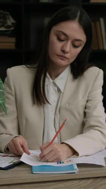 IT uzmanı bir bilişim programı üzerinde çalışmak için çeşitli grafik ve tabloları analiz eder. Kadın programcı not alır ve işyerindeki ofisinde çalışır. Düşünceli ve odaklanmış bir kadın.