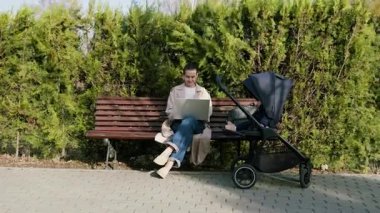 Bebekler bebek arabasında oturup uyurken bilgisayardan uzaktan e-posta yazan serbest çalışan genç bir kadın. Annem doğum iznindeyken parkta çalışıyor.