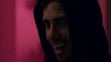 Kapüşonlu bir hacker 'ın tehlikeli yüzü gülerken, dizüstü bilgisayarda klavye yazarken ve şifreleri kırarken. Tehlikeli kapüşonlu bilgisayar korsanı sisteme siber virüs bulaştırıyor..