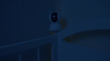 Bebek beşiğinden sarkan güvenlik kamerası geceleri uyurken bebeklerin uyumasını izliyor ve gözetliyor. Telefondaki uygulamayla kablosuz internet üzerinden dijital cihaz. Güvenlik ve güvenlik.