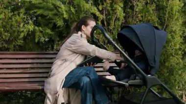 Bebek arabasında bebeğe bakarken parkta tablet üzerinde çalışan genç bir iş kadını. Annelik ve iş hayatını birleştiren annelik izninde uzaktan kumandalı internet işinde çalışan güzel bir anne.