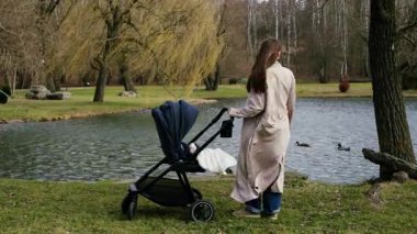 Genç bir kadının göle bakışının arkası. Genç anne, çocuğuyla birlikte parkta bebek arabasıyla yürüyüp anneliğin tadını çıkarıyor..