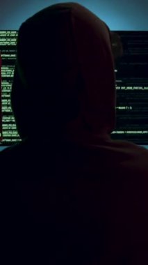 Büyük bilgisayar kulelerinin önünde kapüşonlu bir bilgisayar korsanı, arkadan görüntü, bazı şirketlerin veri platformlarını bozuyor. Klavyede isimsiz bir adam var. Hacker saldırısı, siber güvenlik.