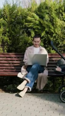 Bebekler bebek arabasında oturup uyurken bilgisayardan uzaktan e-posta yazan serbest çalışan genç bir kadın. Annem doğum iznindeyken parkta çalışıyor.