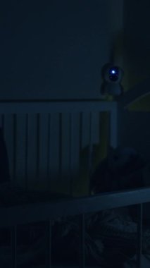 Çocuk odası ve bebek geceleri karyolada uyuyor. Bebeği izleyen bebek beşiğinden sarkan güvenlik kamerası. Wi-Fi ile modern dijital cihaz bebeği izliyor..