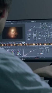 Erkek renkçi karanlıkta bilgisayar monitörleri önünde çalışıyor, renkleri değiştiren bir projede, resimlerin ışıklarıyla çalışıyor. Gözlüklü adam yüksek performans tekniği üzerinde çalışıyor.