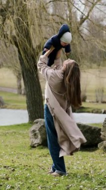Genç anne bebeğini kollarında tutuyor ve onu kaldırıyor ve sıkıca göğsüne sarılıyor. Güzel bir kadın bebeğiyle birlikte rüzgarlı bir bahar günü havuzun kenarında parkta yürür. Mutlu annelik