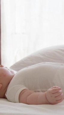 Bir bebek yumuşak bir battaniyeye uzanır, bacaklarını ve kollarını şakaya vurarak hareket ettirir. Güneş ışığı odayı dolduruyor, hareketli bebek bacaklarını sallarken sıcak ve neşeli bir atmosfer yaratıyor.