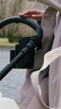 Bebek arabası için bir bardak tutucunun yakın plan görüntüsü. Anne bebeğiyle parkta yürüyor, kahvenin tadını çıkarıyor ve bebek arabasındaki bardak tutacağına koyuyor. Annem işe yarar şeylerle doğum yapmayı sever.