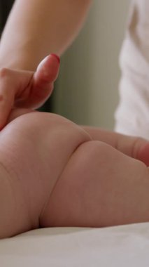 Kimliği belirsiz bir annenin elleri bebek poposuna nazikçe nemlendirici sürüyor ve yeni doğan bebeğe nazikçe masaj yapıyor. Çıplak, rahat bir bebek, yumuşak bir çarşafın üzerinde karnının üzerinde yatıyor.