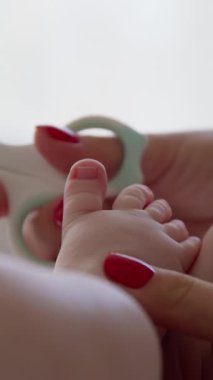 Yeni doğmuş bir bebeğin sabah ışığında çıplak ayakla çekilmiş yakın plan görüntüsü. Annenin elleri bebek rutin bakımını yapıyor ve özel bebek makasıyla bebek tırnaklarını kesiyor..