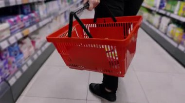 Alışveriş yapan kişi süpermarket koridorunda kırmızı alışveriş sepeti taşıyor. Adam özenle markette taze yiyecek ve ürün arıyor.