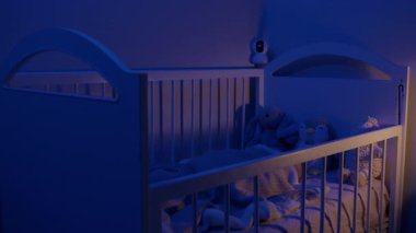 Sakin bebek yumuşak battaniyenin altında peluş hayvanlarla uyur. Kamera, bebek durumunu ve yatak odasındaki davranışları gösteriyor.