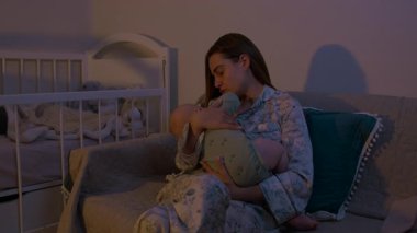 Sevgi dolu anne, gece rahat bir kanepede oturan bebek beşiği besler. Genç kadın, loş aydınlatılmış yatak odasında ninni söyleyen çocukla ilgileniyor.
