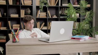 Yorgun adam ev ofisinde kitaplarla ve bitkilerle uğraşarak dizüstü bilgisayara odaklanıyor. Arkaya yaslanan adam odaklanmış çalışma sürecini gösteriyor