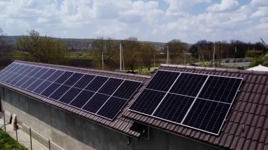 Koyu güneş panelleri, binanın çatısının kiremitli bölümlerine belirgin bir şekilde yerleştirilmiş. Bulutlu gökyüzünün altında ticari yenilenebilir enerji kurulumu