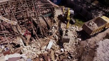 Kazı makinesi çökmüş binadan dökülen enkazı temizliyor. Yıkım sürecinden kalma tuğlalarla ve yapısal kalıntılarla dolu bir alan