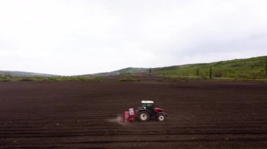 Kırmızı traktör tohum eker. Alacakaranlıkta bulutlu gökyüzünün altında yeni ekilmiş geniş tarlalara tohum eker. Modern tarımın özü