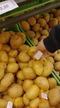 Müşteri alışveriş gününde marketin rafından çiğ patates topluyor. Adam markette taze sebze filesini dikkatlice alıyor.