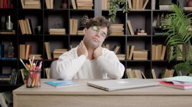 Genç adam saatlerce çalıştıktan sonra rahatsız hissederken ofisinde oturup boyun masajı yapıyor. Adam rahatlamak için gözlüğünü çıkarıyor.