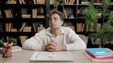 Genç öğrenci kütüphanede masasında gözleri kapalı kısa bir şekerleme yapar. Adam elleriyle boynunu uzatıyor. Yorgun ve dinlenmeye ihtiyacı var.