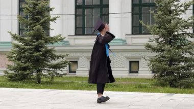 Yüksek lisans öğrencisi şapkasını çıkararak üniversite binasına doğru dönüyor. Adam büyük tarihi binaya neşeyle el sallıyor.