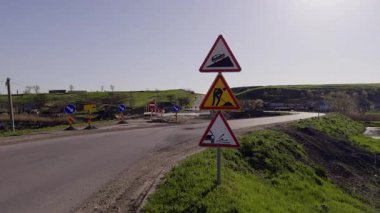 Üçgen yol işaretleri, inşaat tümseği ve heyelan uyarısı için köy hendeğinin kenarında duruyor. Güneşli ışık eğimi ve boş dönüşü kapatır