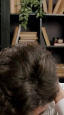 Adam gözlerini kapatıyor ve kitaplığa karşı oturarak işten sonra ellerini boynuna bastırıyor. İfade barışçıl çalışma bölgesinde gerginliğin azaldığını gösteriyor