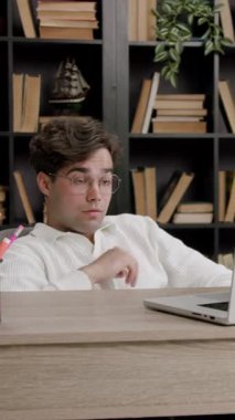 Yorgun adam ev ofisinde kitaplarla ve bitkilerle uğraşarak dizüstü bilgisayara odaklanıyor. Arkaya yaslanan adam odaklanmış çalışma sürecini gösteriyor