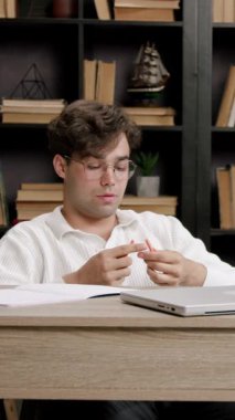 Masadaki ciddi öğrenci kalemi dikkatle inceliyor. Adam sakin kalıyor ve bilgisayarla masa başında kısa bir ara vermeye odaklanıyor.