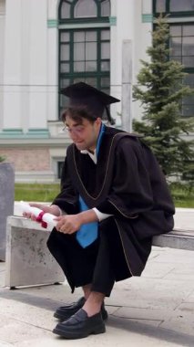 Adam elinde diplomayla taş bir bankta oturuyor ve gerçeğe inanmıyor. Mezuniyet cüppesi insan vücudunu tarihi yapıya karşı kumaşla kaplıyor.