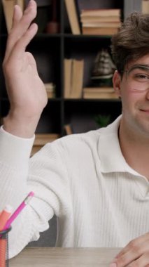 Kendine güvenen erkek öğrenci kütüphanenin merkez ofisinde masa başında otururken elini kaldırıyor. Soruya cevap vermeye çalışan zeki ve dost canlısı birine benziyor.