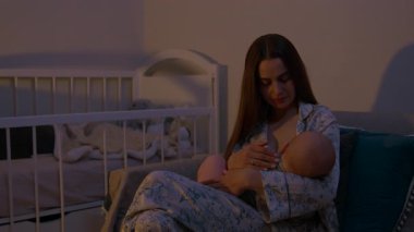 Genç anne yeni doğmuş bebeği koltukta rahatça oturarak emziriyor. Bebekli bir kadın huzurlu bir annelik sahnesi sergiliyor.