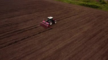 Traktör, ekiciyi yeni sürülmüş büyük kahverengi araziye çeker. Makine aktif ekimi gösteren toprak üzerinde belirgin düz çizgiler bırakır
