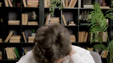 Adam gözlerini kapatıyor ve kitaplığa karşı oturarak işten sonra ellerini boynuna bastırıyor. İfade barışçıl çalışma bölgesinde gerginliğin azaldığını gösteriyor