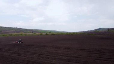 Kırmızı traktör, ekime hazırlanan tarla üzerinde kara toprak sürüyor. Bahar günü tepeleri olan verimli topraklarda düz çizgiler.