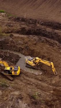 Kazıcılar toprak taşıma operasyonları sırasında inşaat alanında yeşillik olan çamurlu bölgede çalışırlar. Makineler siper şekillendirme manzarası kazıyor