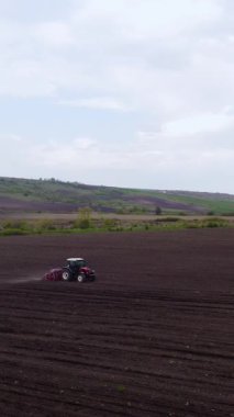 Kırmızı traktör, ekime hazırlanan tarla üzerinde kara toprak sürüyor. Bahar günü tepeleri olan verimli topraklarda düz çizgiler.
