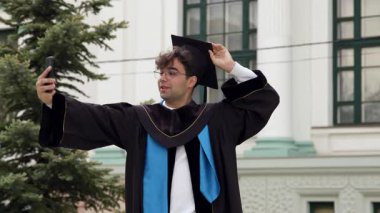 Happy Mezun 'un elinde geleneksel havan panosunu ayarlayan bir video kaydı var. Önlüklü öğrenci, üniversite binasının yanında köknar ağacıyla duruyor.