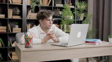 Odaklanmış genç öğrenci dizüstü bilgisayar ekranına bakarken el ele tutuşuyor. Dekoratif unsurlara sahip raflar barış ortamını şekillendirir