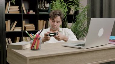 Genç adam heyecan verici bir şekilde masa başında bilgisayar ve eğitimi umursamadan joystick oynuyor. Adam oyalanma ve video oyunlarına bağımlılık gösteriyor.