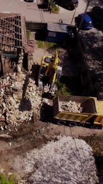 Yıkım kazıcısı eski binanın çatısından dökülen parçaları çöp kamyonuna yüklüyor. Yıkım alanındaki kırık malzemeleri bekleme kamyonuna boşaltıyorum.