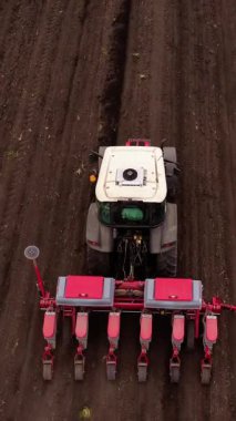 Tarım makinesi geniş kahverengi alanda çalışır ve toprakta paralel çizgiler oluşturur. Çekici, yerleştirme sürecini genişletmek için hareket eder