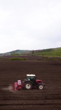 Kırmızı traktör tohum eker. Alacakaranlıkta bulutlu gökyüzünün altında yeni ekilmiş geniş tarlalara tohum eker. Modern tarımın özü