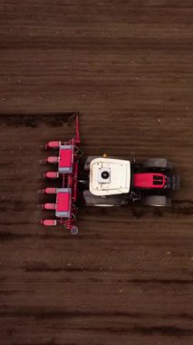 Çekici, kırmızı bitkiyi engin kahverengi alanda çeker ve toprakta paralel çizgiler yaratır. Uzun gölgeli bitkiler toprağa uzanıyor.