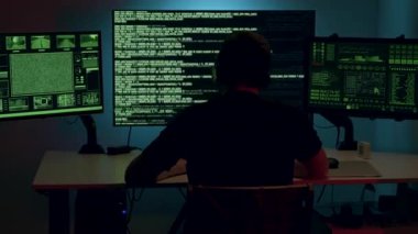 Arkadan, kafasında kulaklıkla bilgisayar monitörlerinin önünde birkaç veri platformuna girip bilgi çalıyor. İsimsiz adam çeşitli virüsler tanıtıyor.