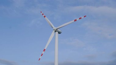 Kırmızı ve beyaz bıçaklı uzun rüzgar türbini, temiz enerji çözümleri ve sürdürülebilir teknolojideki gelişmeleri temsil eden açık mavi gökyüzü üzerinde döner.