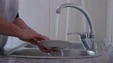 Enfeksiyon önlemedeki temizliğin önemini vurgulamak için temiz bir mutfak lavabosunda akan su ve düzenli bir tezgahla bulaşıkları yıkıyor.