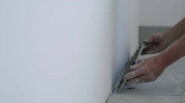 İşçi, çağdaş bir ortamda pürüzsüz doku ve hassasiyeti vurgulayarak, kaliteli işçilik ve adanmışlığı vurgulayarak, duvarlara ustalıkla sıva uygular.