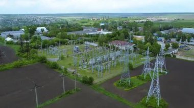 Enerji hatları ve kulelerin bulunduğu, yeşillik ve alanlarla çevrili bir elektrik santralinin hava perspektifi, enerji altyapısının karmaşıklığını vurguluyor.